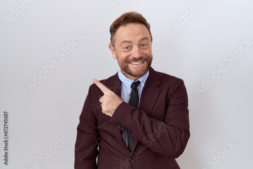 Middle age business man with beard wearing suit and tie cheerful with a smile on face pointing with hand and finger up to the side with happy and natural expression