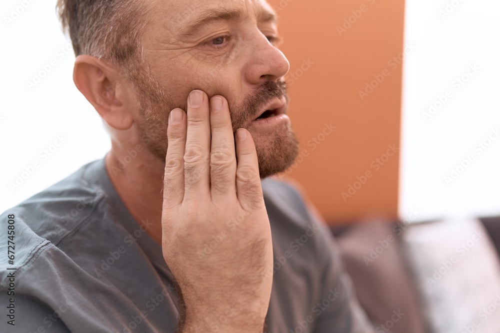 Middle age man suffering for toothache sitting on sofa at home Middle age man suffering for toothache sitting on sofa at home