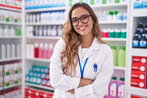 Young beautiful hispanic woman pharmacist smiling confident standing with arms crossed gesture at pharmacy photo