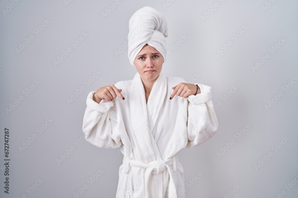 Blonde caucasian woman wearing bathrobe pointing down looking sad and upset, indicating direction with fingers, unhappy and depressed. Blonde caucasian woman wearing bathrobe pointing down looking sad and upset, indicating direction with fingers, unhappy and depressed.