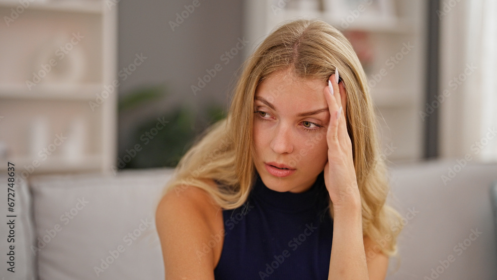 Young blonde woman sitting on sofa with serious expression at home Young blonde woman sitting on sofa with serious expression at home