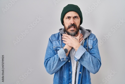 Young hispanic man with tattoos wearing wool cap shouting and suffocate because painful strangle. health problem. asphyxiate and suicide concept.