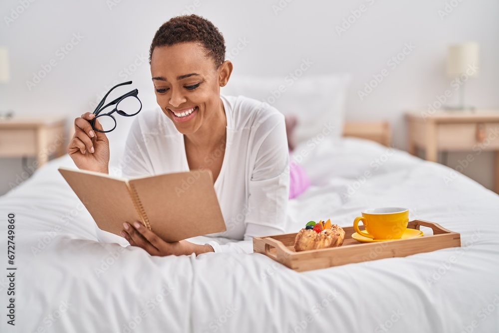 African american woman having breakfast reading book at bedroom