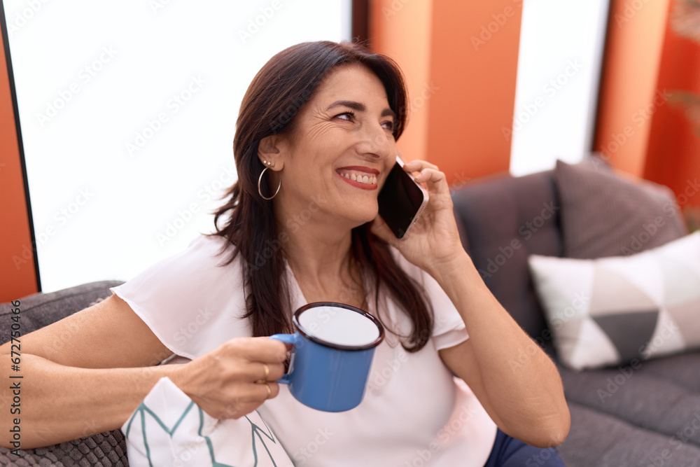 Middle age hispanic woman talking on smartphone drinking coffee at home Middle age hispanic woman talking on smartphone drinking coffee at home