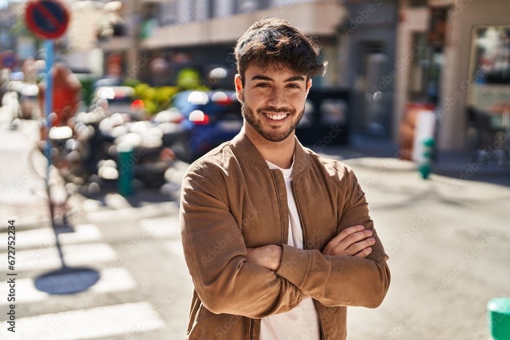 Fototapeta premium Young hispanic man smiling confident standing with arms crossed gesture at street