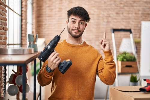 Hispanic man with beard holding screwdriver at new home smiling with an idea or question pointing finger with happy face, number one