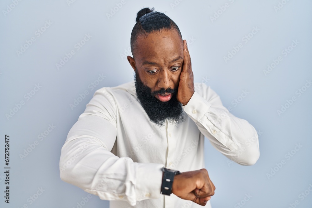 Fototapeta premium African american man standing over blue background looking at the watch time worried, afraid of getting late