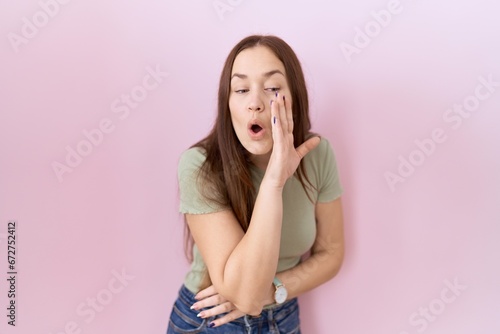 Beautiful brunette woman standing over pink background hand on mouth telling secret rumor, whispering malicious talk conversation