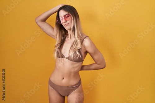 Young hispanic woman wearing bikini over yellow background stretching back, tired and relaxed, sleepy and yawning for early morning