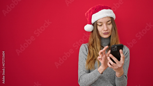 Young caucasian woman wearing christmas hat using smartphone over isolated red background