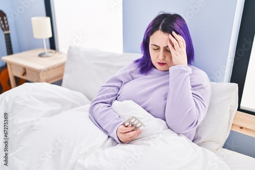 Young beautiful plus size woman taking pills for headache sitting on bed at bedroom