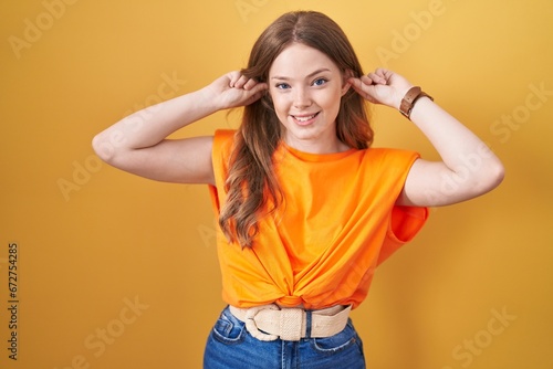 Caucasian woman standing over yellow background smiling pulling ears with fingers, funny gesture. audition problem