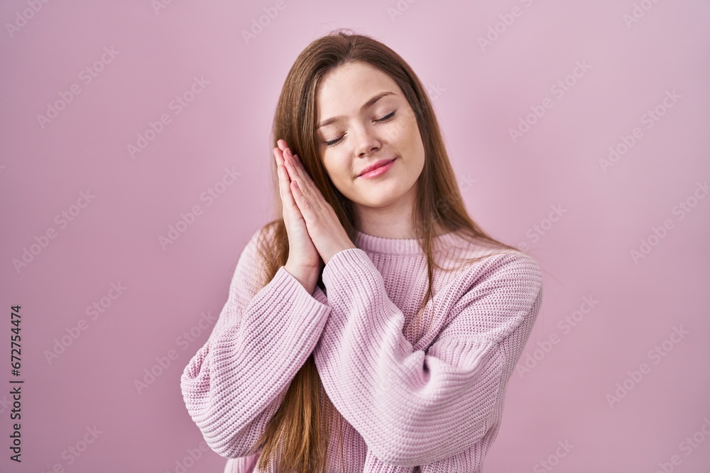 Young caucasian woman standing over pink background sleeping tired dreaming and posing with hands together while smiling with closed eyes. Young caucasian woman standing over pink background sleeping tired dreaming and posing with hands together while smiling with closed eyes.