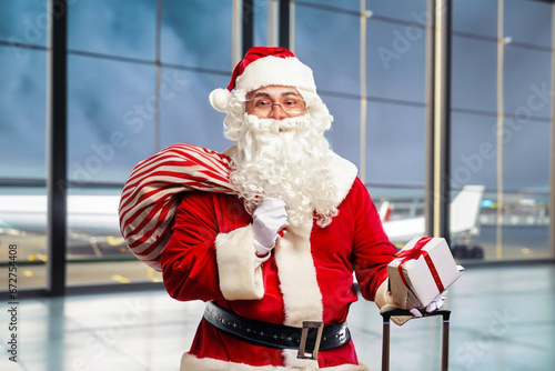 christmas concept at airport holidays with happy smiling santa claus with gifts