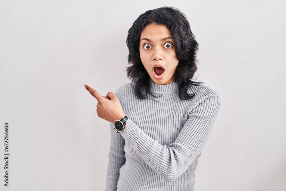 Hispanic woman with dark hair standing over isolated background surprised pointing with finger to the side, open mouth amazed expression. Hispanic woman with dark hair standing over isolated background surprised pointing with finger to the side, open mouth amazed expression.