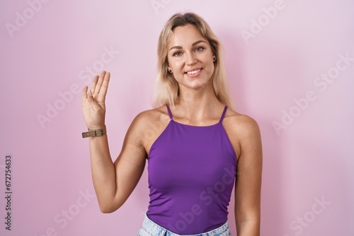Young blonde woman standing over pink background showing and pointing up with fingers number four while smiling confident and happy. © Krakenimages.com