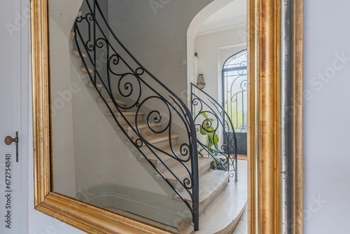 Luxurious gold framed mirror elegantly mounted onto a wooden banister near a staircase