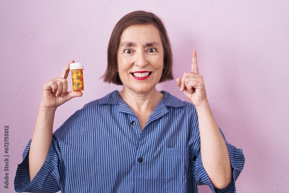 Middle age hispanic woman holding pills surprised with an idea or question pointing finger with happy face, number one Middle age hispanic woman holding pills surprised with an idea or question pointing finger with happy face, number one