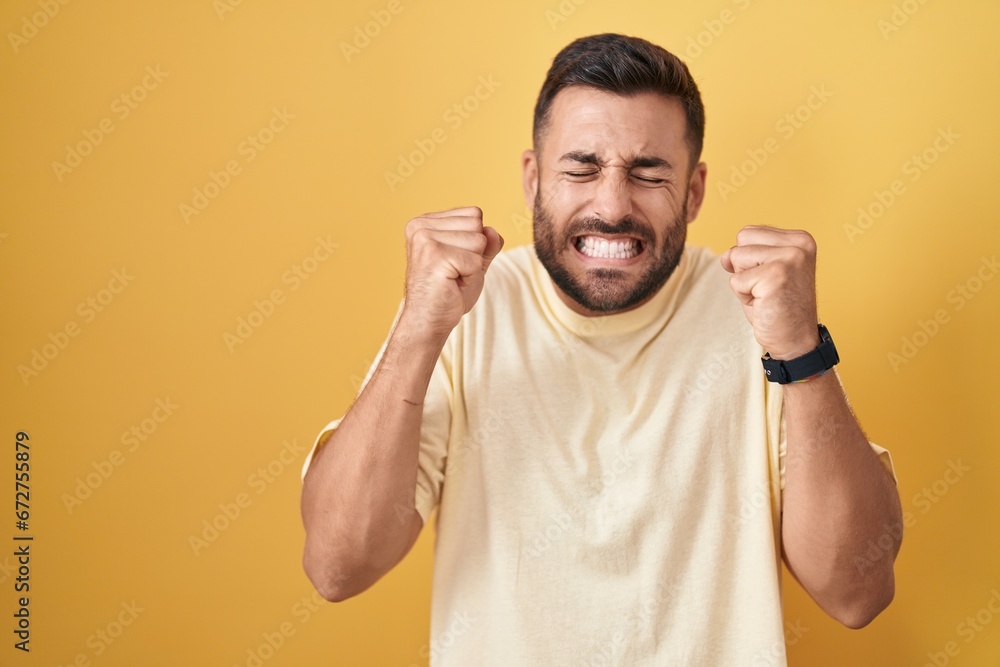 Handsome hispanic man standing over yellow background excited for success with arms raised and eyes closed celebrating victory smiling. winner concept. Handsome hispanic man standing over yellow background excited for success with arms raised and eyes closed celebrating victory smiling. winner concept.