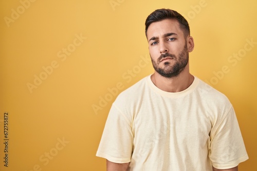 Handsome hispanic man standing over yellow background looking sleepy and tired, exhausted for fatigue and hangover, lazy eyes in the morning.