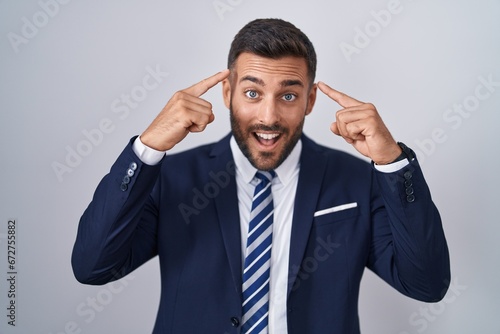 Handsome hispanic man wearing suit and tie smiling pointing to head with both hands finger, great idea or thought, good memory