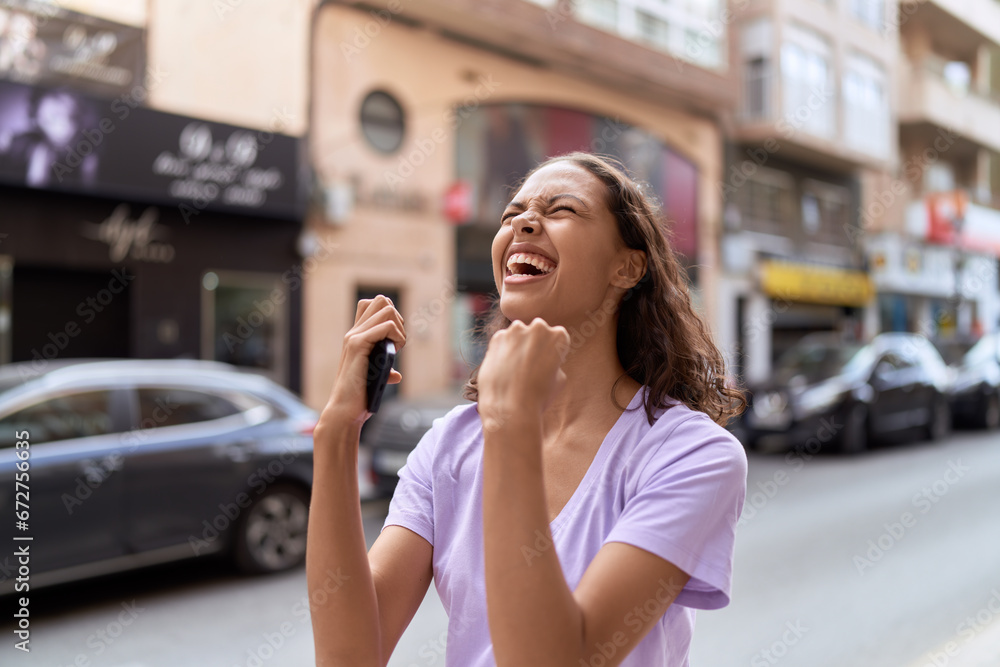 Young african american woman using smartphone with winner expression at street Young african american woman using smartphone with winner expression at street