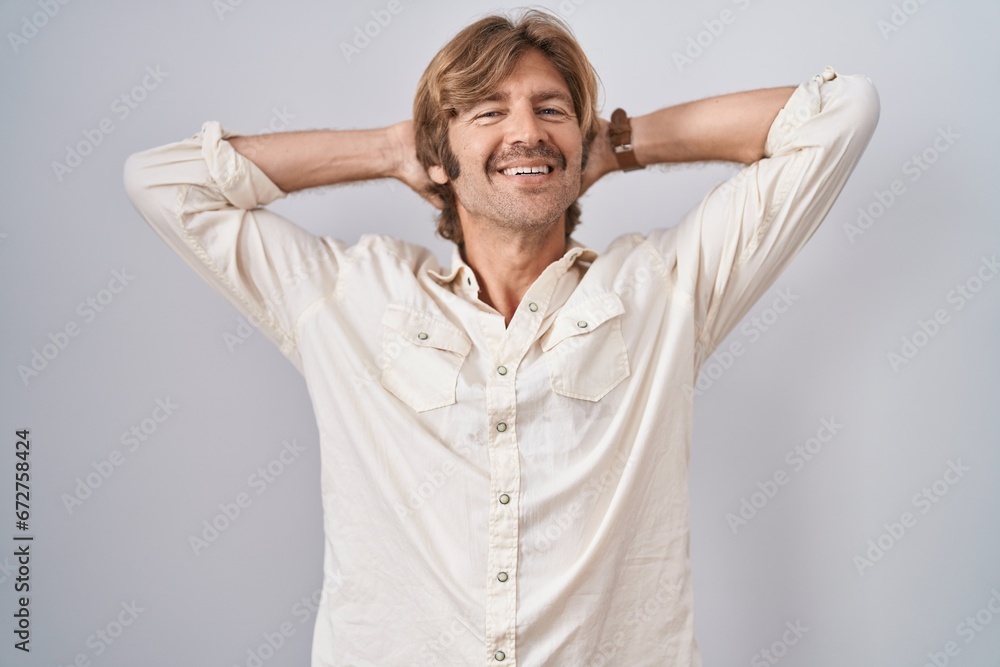 Middle age man standing over isolated background relaxing and stretching, arms and hands behind head and neck smiling happy Middle age man standing over isolated background relaxing and stretching, arms and hands behind head and neck smiling happy
