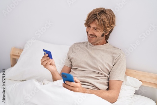 Young man using smartphone and credit card sitting on bed at bedroom photo