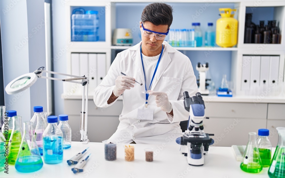 Young hispanic man scientist holding sample with tweezer at laboratory Young hispanic man scientist holding sample with tweezer at laboratory