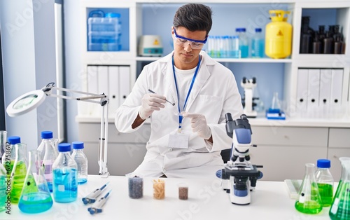 Young hispanic man scientist holding sample with tweezer at laboratory
