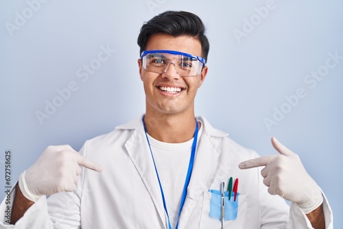 Hispanic man working as scientist looking confident with smile on face, pointing oneself with fingers proud and happy.