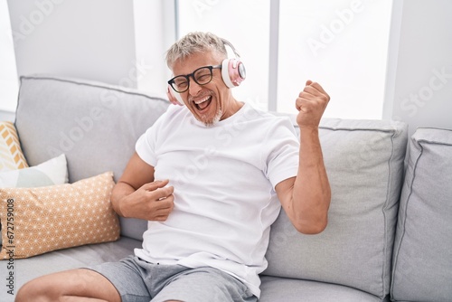 Middle age grey-haired man listening to music doing guitar gesture at home