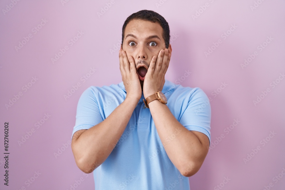 Hispanic man standing over pink background afraid and shocked, surprise and amazed expression with hands on face Hispanic man standing over pink background afraid and shocked, surprise and amazed expression with hands on face