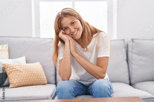 Young blonde girl smiling confident sitting on sofa at home