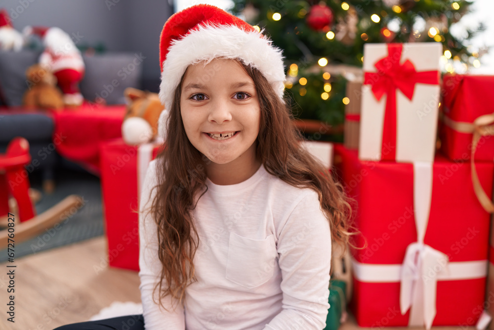 Adorable hispanic girl smiling confident sitting on floor by christmas tree at home Adorable hispanic girl smiling confident sitting on floor by christmas tree at home