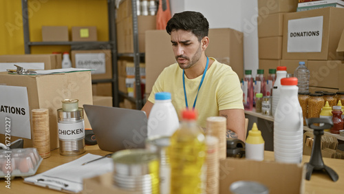 Young hispanic man volunteer using laptop with serious face at charity center