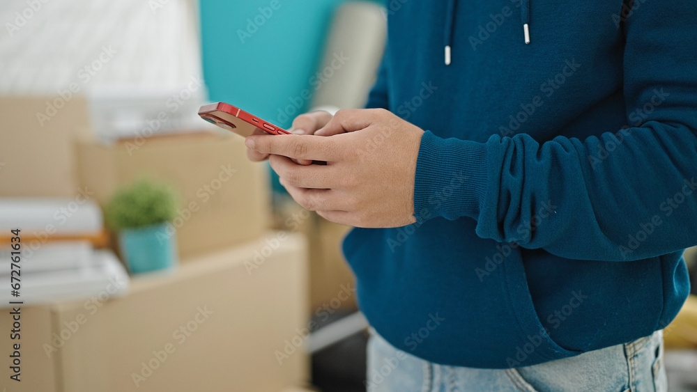 Young hispanic man using smartphone at new home