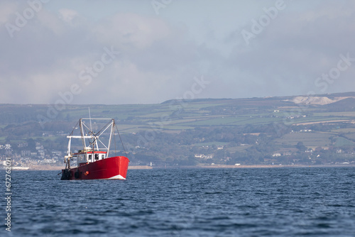 A bright red fishing trawler out to sea on the coast of Cornwall. © Migara