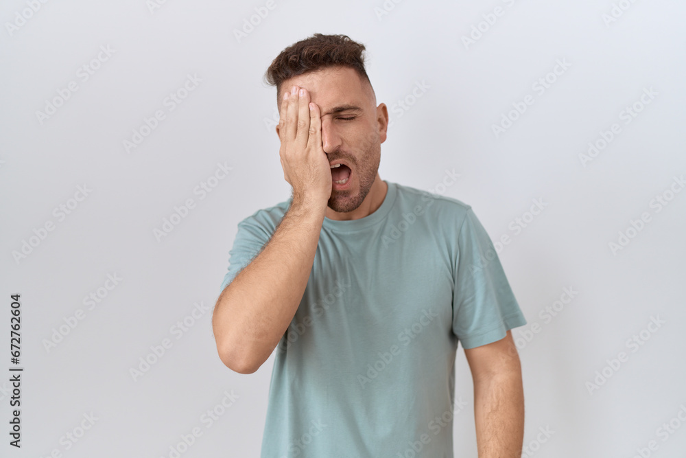 Hispanic man with beard standing over white background yawning tired covering half face, eye and mouth with hand. face hurts in pain. Hispanic man with beard standing over white background yawning tired covering half face, eye and mouth with hand. face hurts in pain.