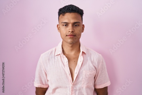 Young hispanic man standing over pink background relaxed with serious expression on face. simple and natural looking at the camera. © Krakenimages.com
