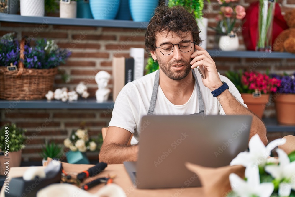 Young hispanic man florist talking on smartphone using laptop at flower shop Young hispanic man florist talking on smartphone using laptop at flower shop