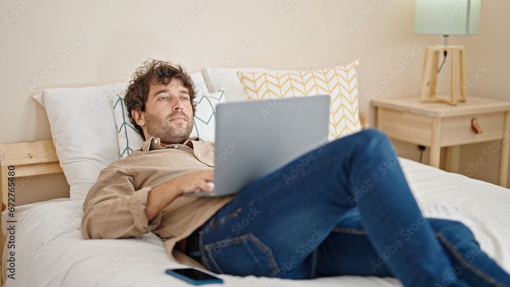Young hispanic man using laptop lying on bed at bedroom Young hispanic man using laptop lying on bed at bedroom