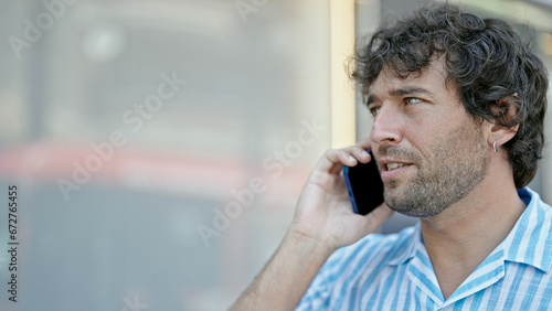 Young hispanic man talking on smartphone with serious expression at street