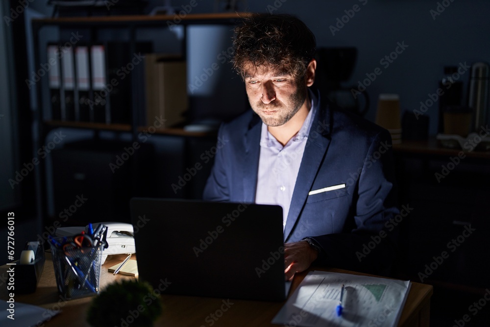Hispanic young man working at the office at night puffing cheeks with funny face. mouth inflated with air, crazy expression. Hispanic young man working at the office at night puffing cheeks with funny face. mouth inflated with air, crazy expression.