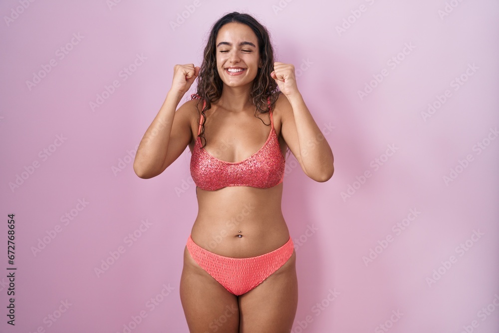 Obraz premium Young hispanic woman wearing lingerie over pink background excited for success with arms raised and eyes closed celebrating victory smiling. winner concept.