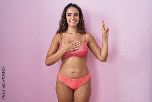 Young hispanic woman wearing lingerie over pink background smiling swearing with hand on chest and fingers up, making a loyalty promise oath