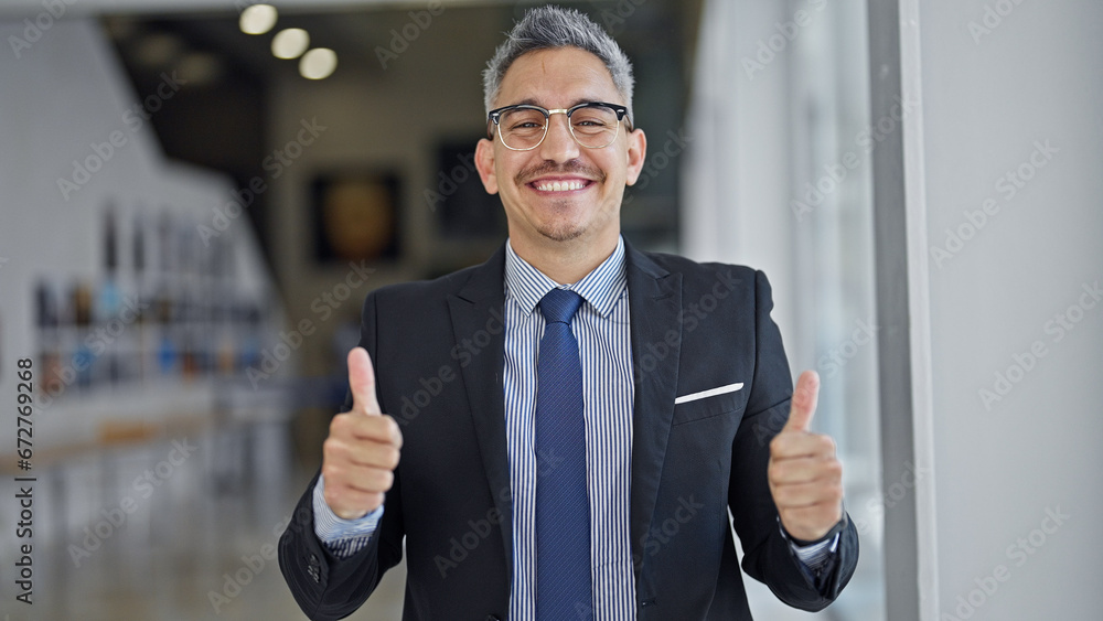 Young hispanic man business worker smiling confident doing thumbs up gesture at office