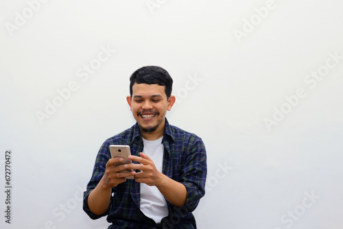 Adult Asian man clenched fist while holding smartphone and showing happy and enthusiastic expression photo