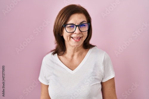 Middle age hispanic woman standing over pink background winking looking at the camera with sexy expression, cheerful and happy face.