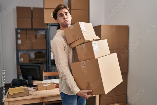 Young man working at small business ecommerce holding packages puffing cheeks with funny face. mouth inflated with air, catching air. © Krakenimages.com